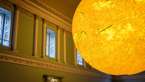 A photo of the Helios art installation which is a giant yellow ball suspended in the Bath Assembly Rooms